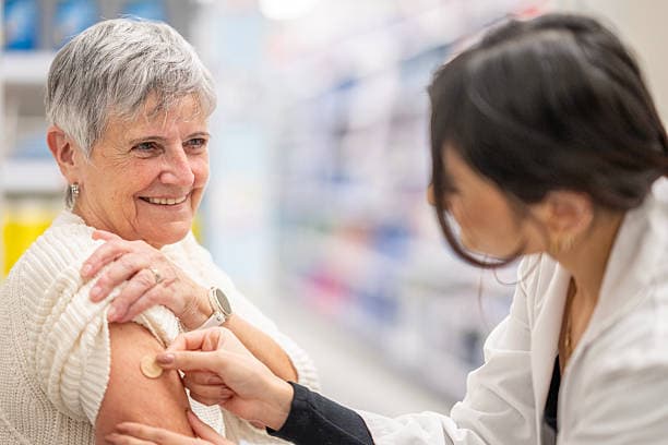 Une pharmacienne administre un vaccin à une patiente souriante, au comptoir de l'officine